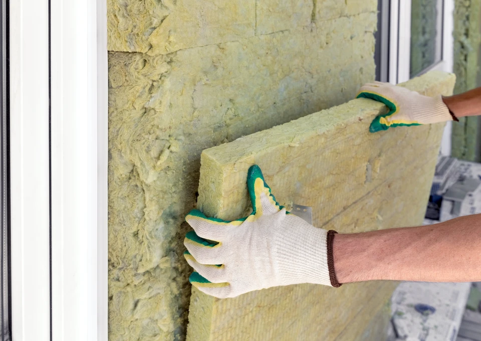 Ouvrier en combinaison de protection intégrale et masque respiratoire installant de l'isolant dans les combles d'une habitation